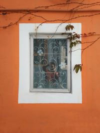 Man photographing with mobile phone while reflecting window amidst orange wall