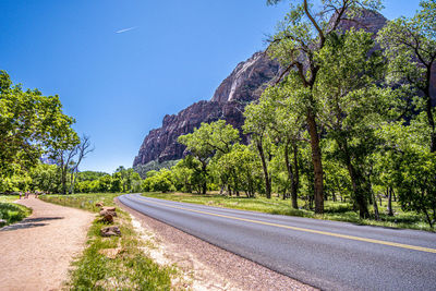 Road amidst trees against clear blue sky