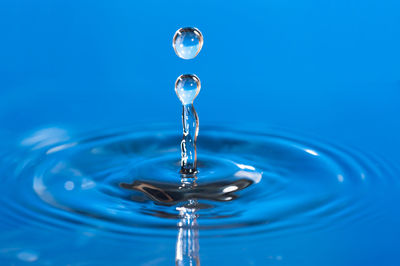 Close-up of drop falling on water against blue background