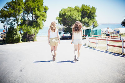 Rear view of young women walking on road leading towards beach