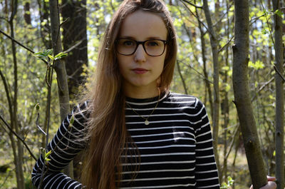 Portrait of beautiful young woman standing against trees