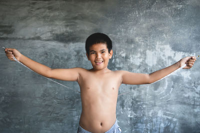 Portrait of cheerful boy holding measuring tape while standing against wall