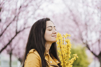 Portrait of woman with pink flower against trees