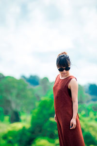 Young woman wearing sunglasses standing on mountain against cloudy sky