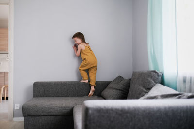Child jumps and plays on sofa in minimalist living room, gray sofa.