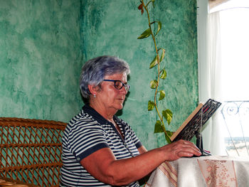 Woman reading book while sitting by window at home