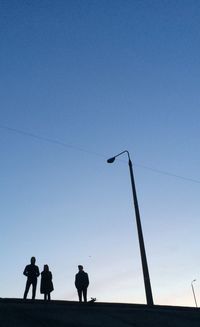 Low angle view of silhouette people standing on beach against clear blue sky
