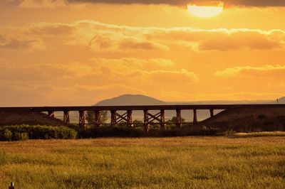 Bridge over field against sky during sunset