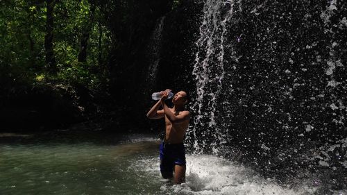 Full length of shirtless man standing in forest