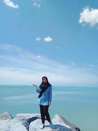 Portrait of smiling woman standing on rocks by sea against sky