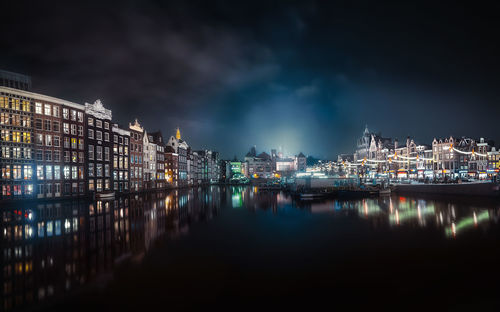 Illuminated buildings by river against sky in city at night