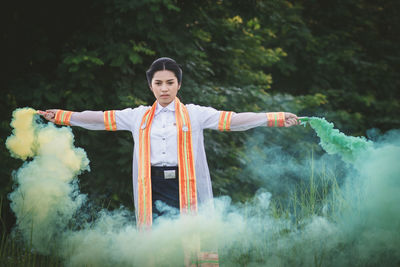 Portrait of woman holding distress flare while standing on field