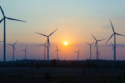 Windmills on land against sky during sunset