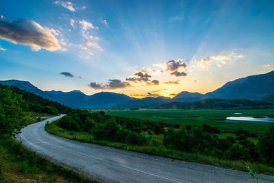 Scenic view of road by mountains against sky during sunset