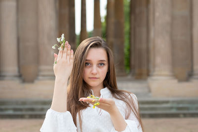 Portrait of young woman holding flowers standing outdoors