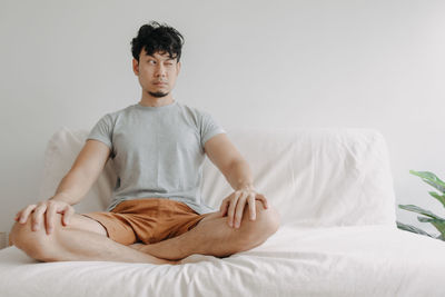 Man winking while sitting cross-legged on sofa at home