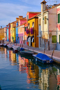 Boats moored in canal by buildings against sky in city