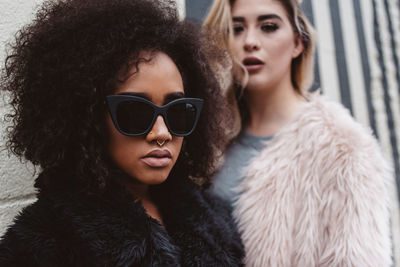 Portrait of woman in sunglasses and fur coat with friend against wall