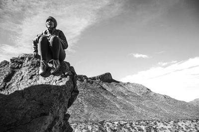 View of woman sitting on rocky landscape against sky