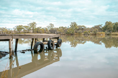 Pier with reflection of trees on river against sky