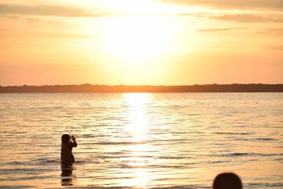 Girl standing in sea against sky during sunset