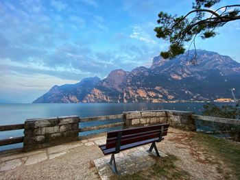 Empty bench by sea against sky