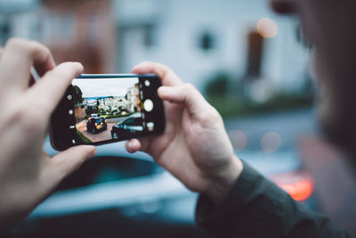 Cropped image of man photographing car through mobile phone