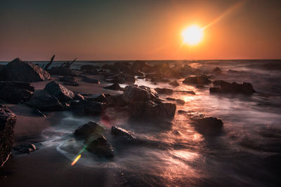 Rocks at beach against sky during sunset