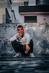 Portrait of young man sitting by wall outdoors