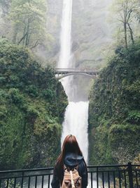 Rear view of woman standing against waterfall