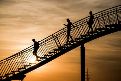 Silhouette man walking on footbridge against sky