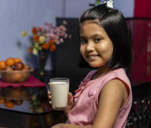 Head shot of a cute little indian / asian girl holding a glass full of milk with smiling face 