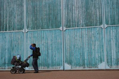 Side view of man standing with baby stroller against blue wall