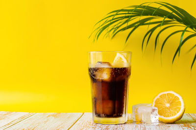 A glass of cold soft drink with lemon on wooden floor with coconut leaf. summer drink concept.