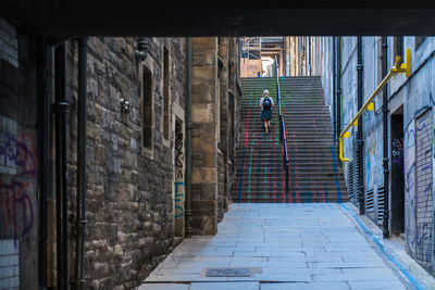 Rear view of woman climbing steps amidst buildings in city