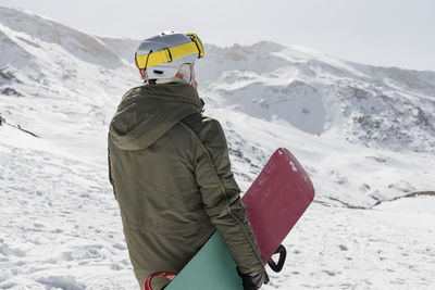 Young man with snowboard standing on snowcapped mountain