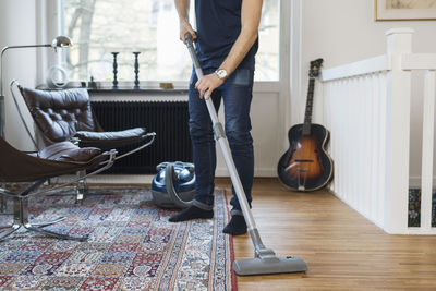 Low section of man vacuuming floor at home