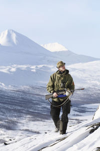 Man with umbrella on snowcapped mountain against sky