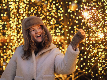 Portrait of young woman standing against illuminated christmas