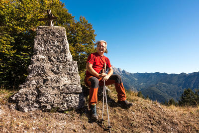 Portrait of man sitting on rock against clear blue sky