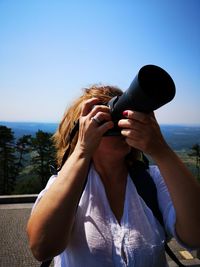 Woman photographing while standing on mountain against clear sky