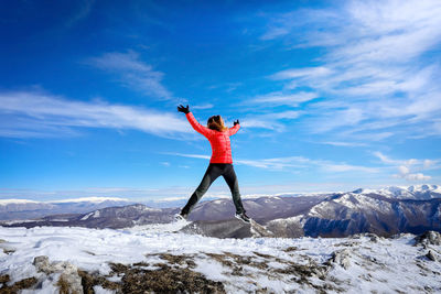 Hiker on top of the mountain happily jumps in front of the horizon of mountain ranges