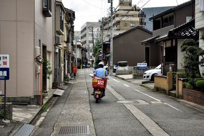 Rear view of man riding motor scooter on road in city