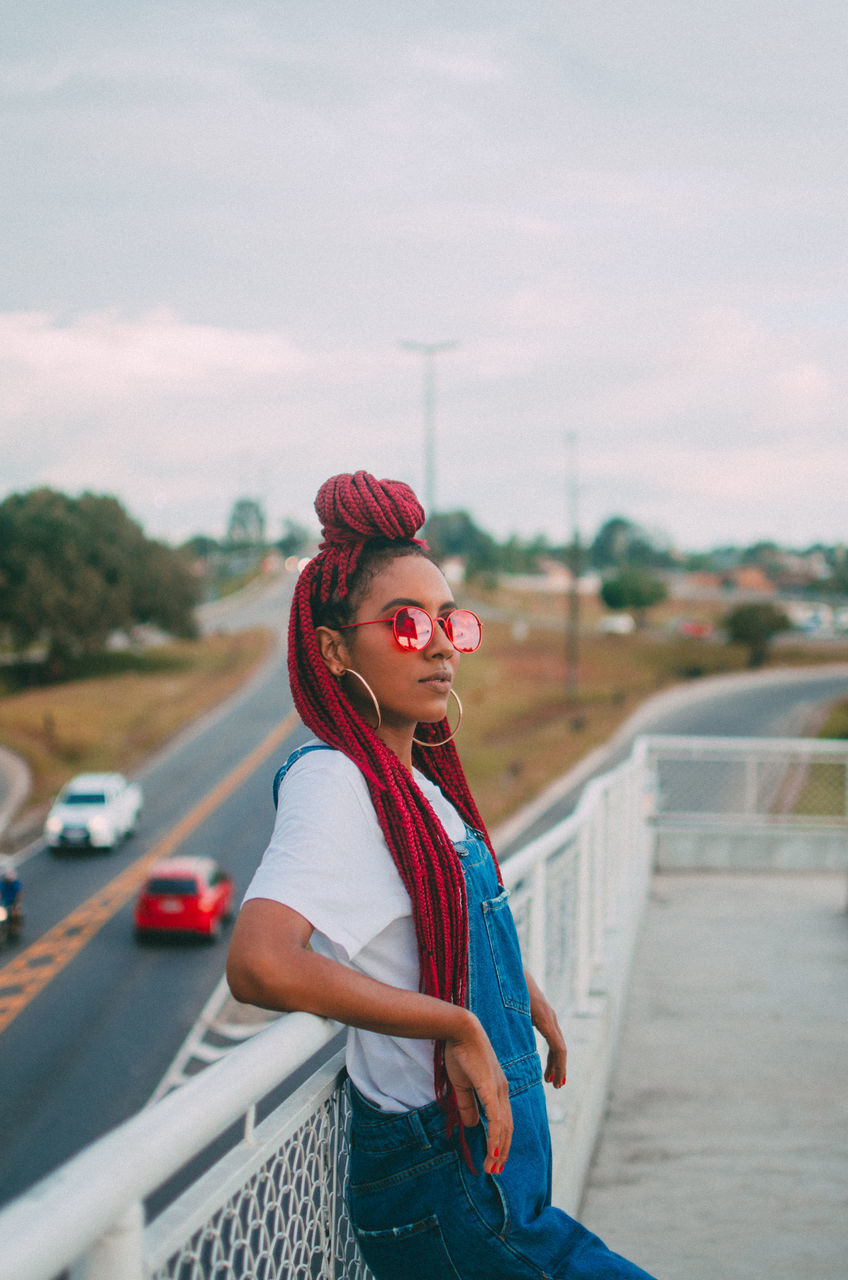 young adult, one person, real people, lifestyles, transportation, focus on foreground, leisure activity, standing, casual clothing, architecture, young women, city, sky, day, road, side view, three quarter length, waist up, outdoors, hairstyle, teenager