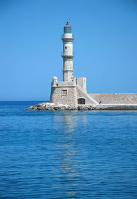 Lighthouse by sea against clear sky