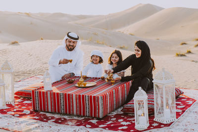 Happy family having tea on carpet at desert
