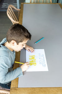 Little kid drawing stop war on a paper. ukraine russia war concept.