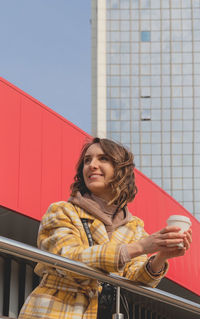 Happy caucasian woman in a yellow coat with cup of coffee to go on city walk.