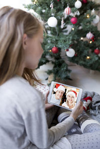 Girl video conferencing while holding digital tablet by christmas tree