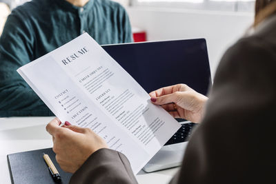 Hands of recruiter holding resume in front of candidate at desk